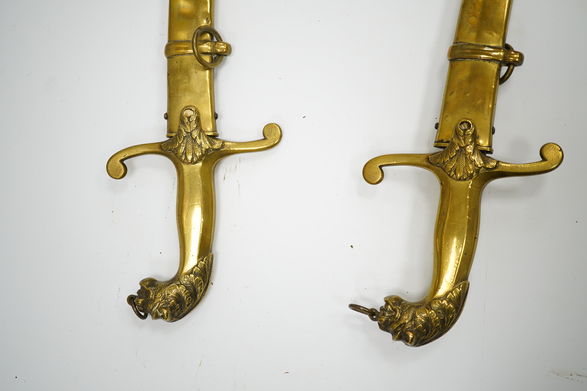 A pair of Victorian bandsman’s swords of Shamshir type, curved single edge blades, cast brass hilts with lions head pommels, in their brass scabbards. Condition - good, some dents to scabbards.